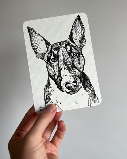 Hand holding a card with a black and white illustration of a dog portrait against a plain background