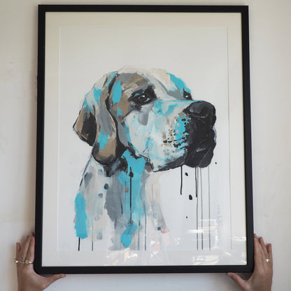 Framed artwork of a dog portrait with abstract blue and grey design held by two hands against a white wall.