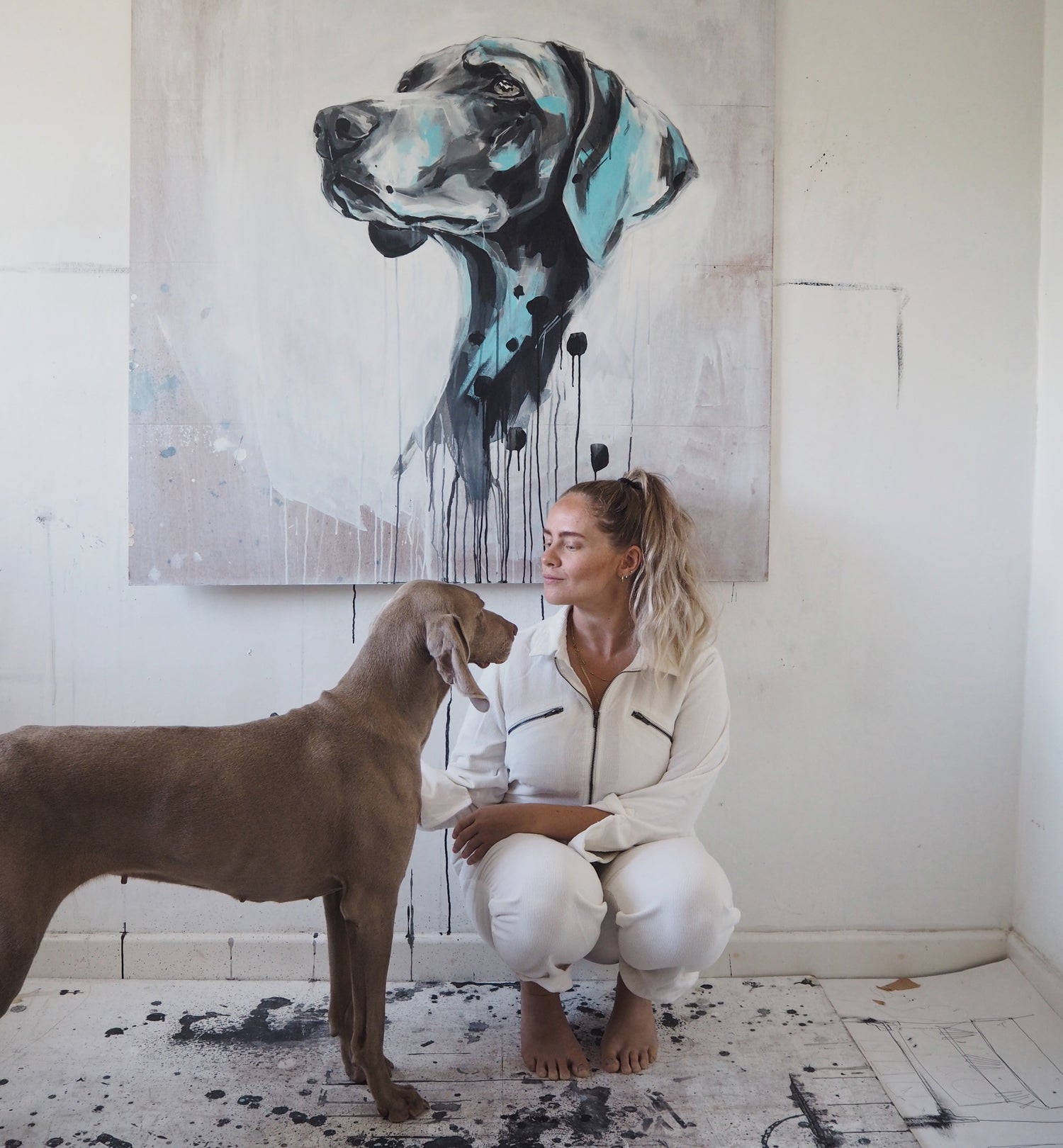 woman with a Weimaraner in front of a large abstract painting of a dog portrait
